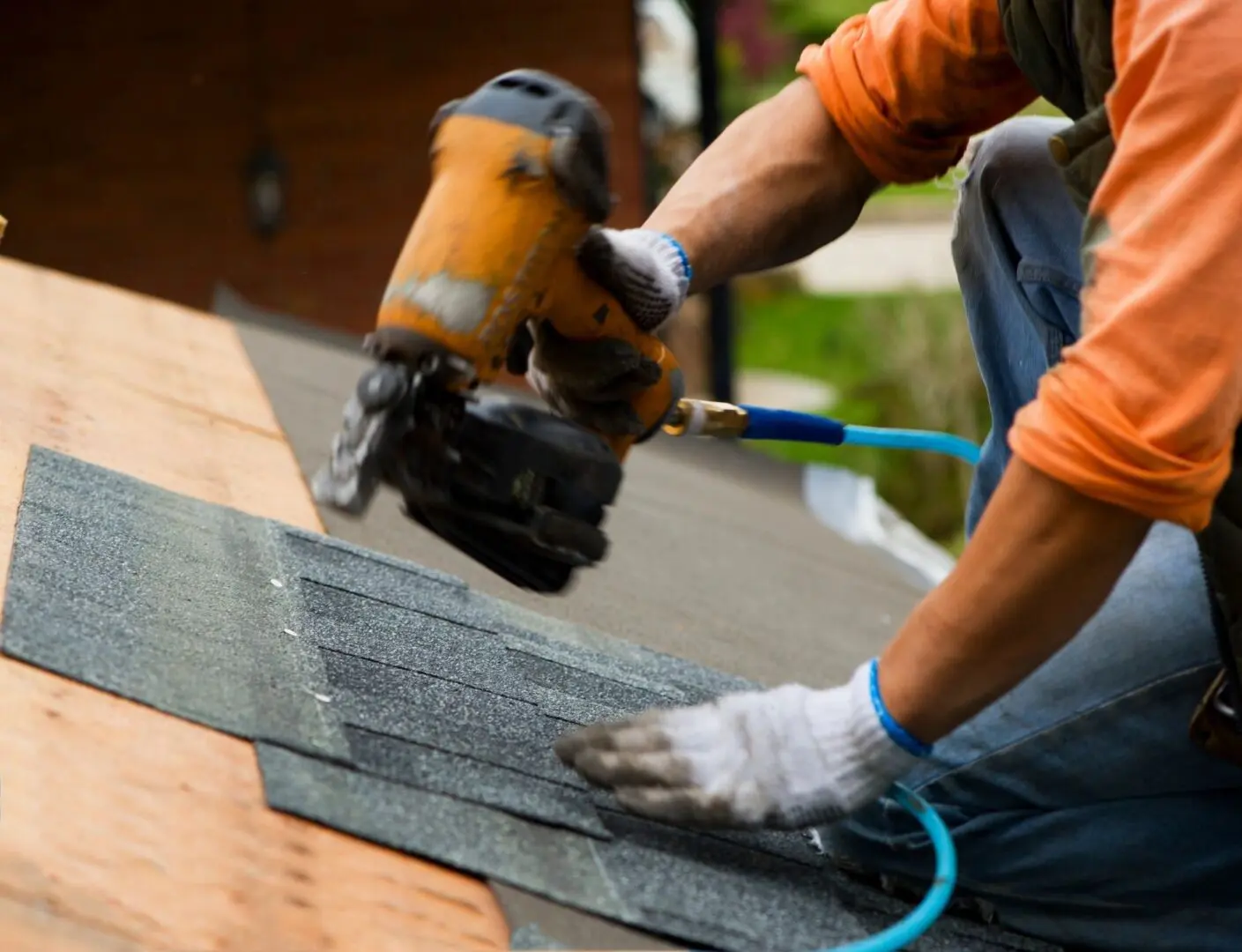 A person with gloves on working on the roof of a house.